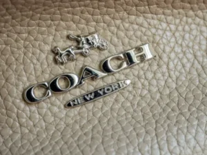 Detalhe do logotipo Coach em couro, evidenciando uma marca internacional de moda reconhecida por acessórios e roupas de alto padrão.