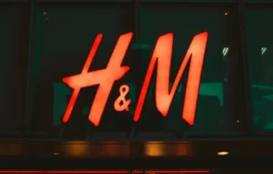 Logotipo iluminado da H&M em vermelho na fachada de loja, representando marca de roupas famosa do varejo de moda acessível e presença global.