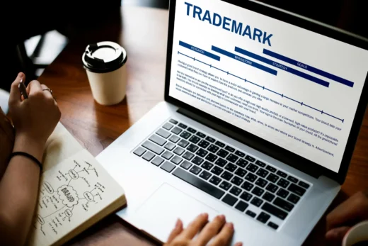 Pessoa planejando estratégia de trademark em notebook, com anotações e café sobre mesa de trabalho.